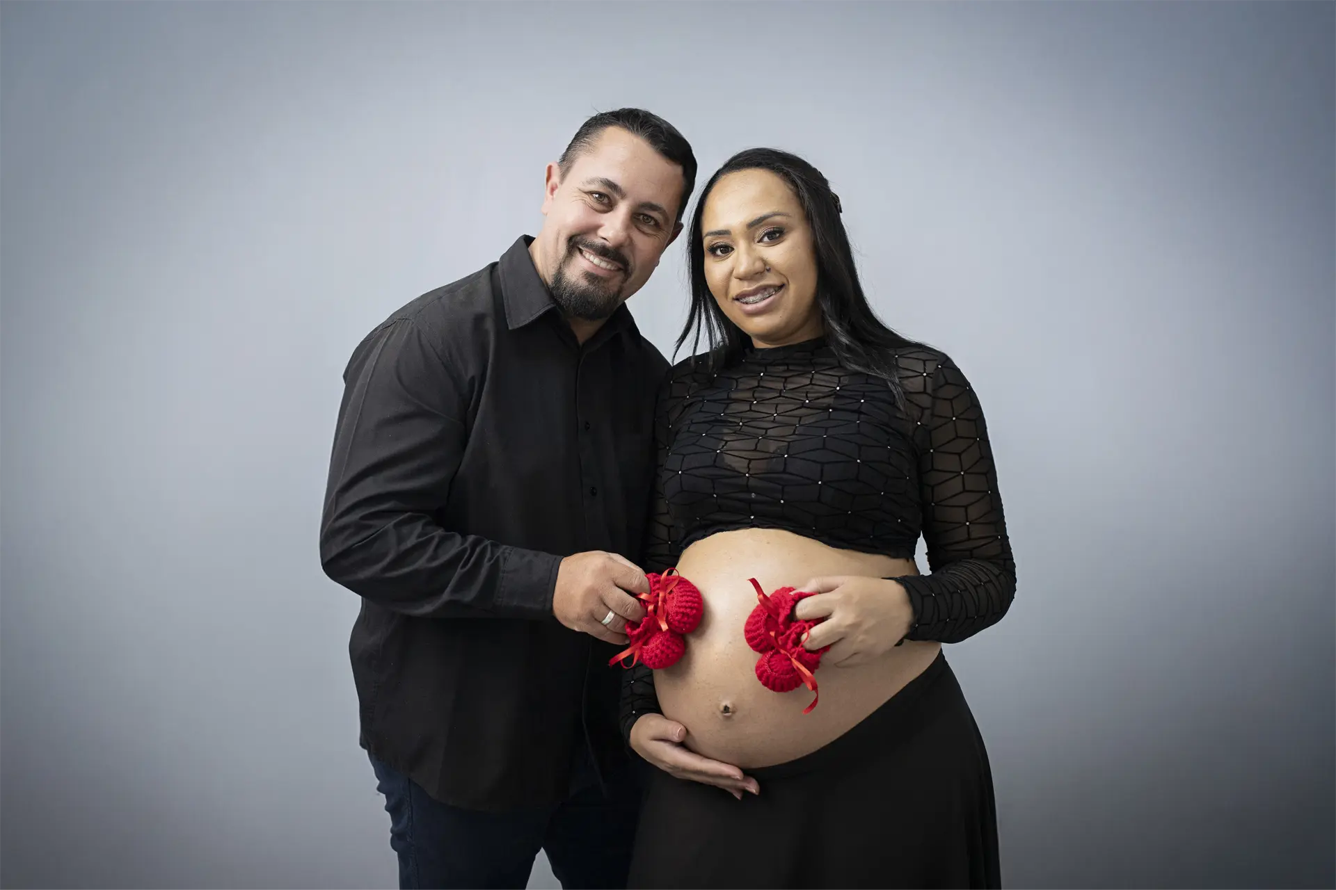 Casal segurando sapatinhos vermelhos de bebê sobre a barriga da gestante