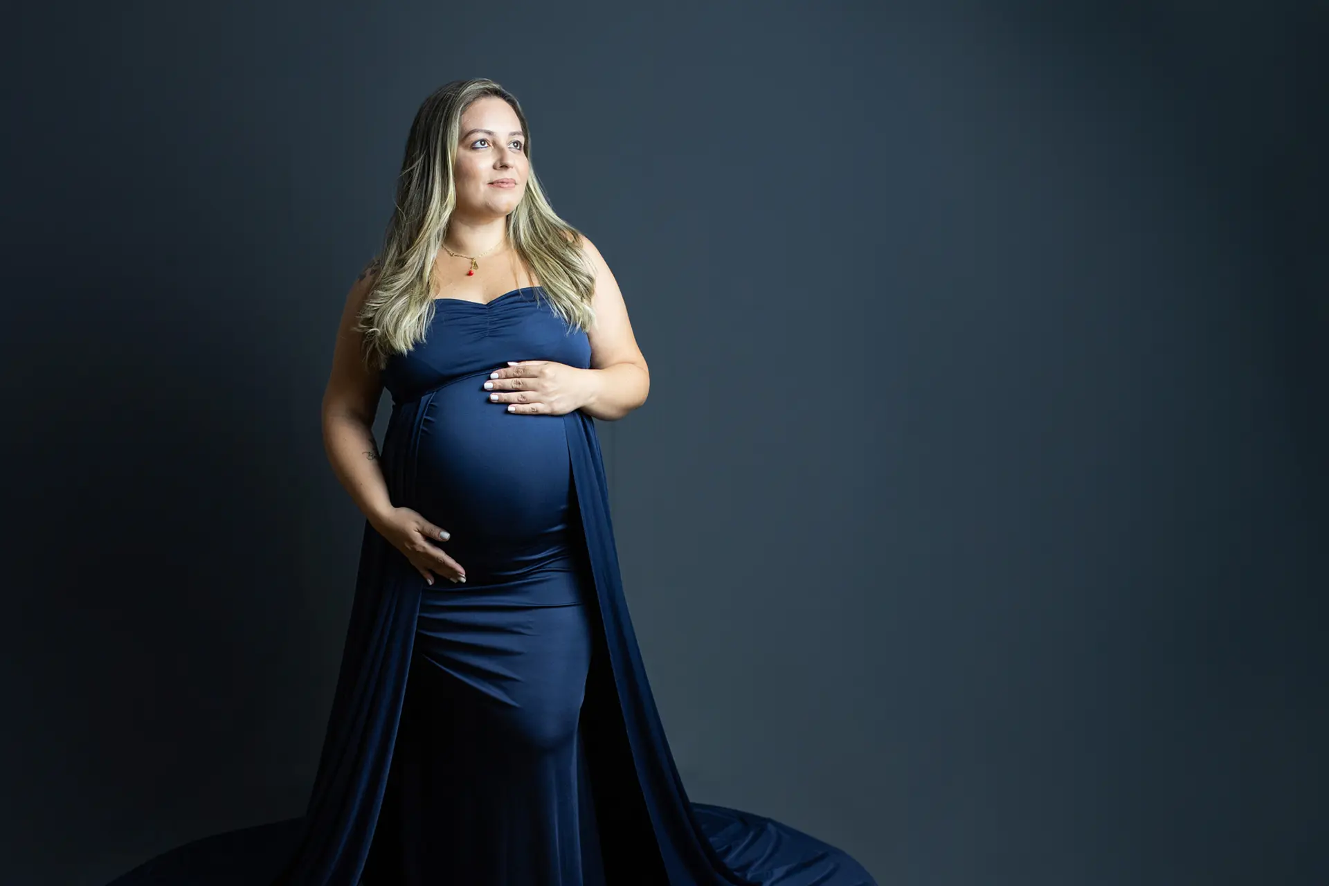 Gestante em vestido longo azul-marinho em ensaio de estúdio