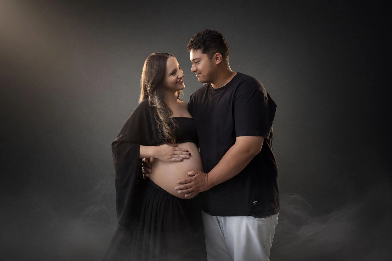 Casal sorridente em ensaio gestante, ele com as mãos na barriga dela